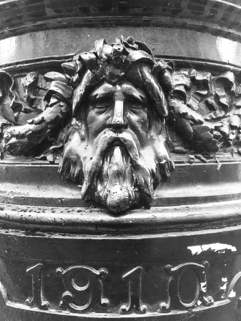 A black and white photo of the green man cat in iron as part of a lamppost on London’s embankment.