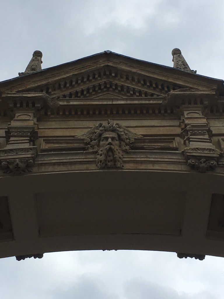 A photo of a stone arch featuring a central carved face against a grey sky