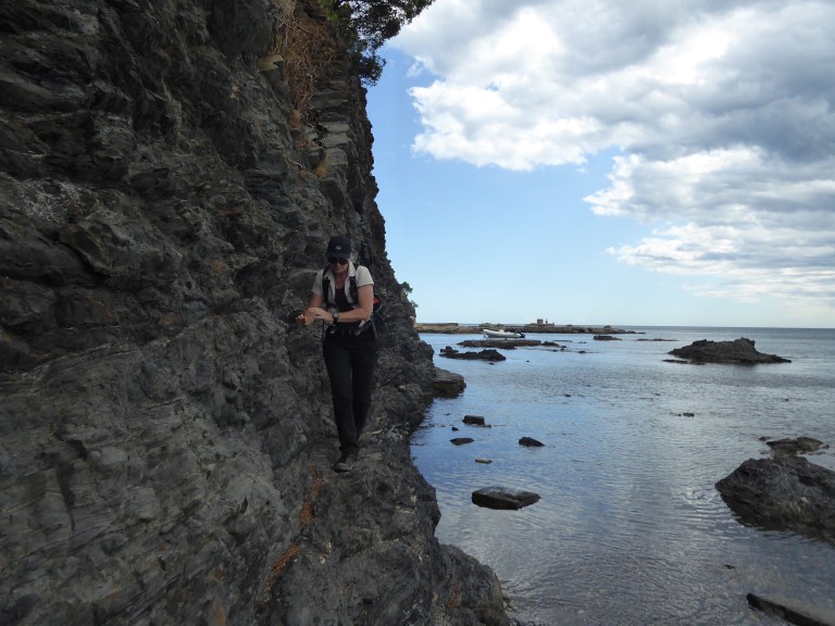 A photo of a person walking along the base of a cliff next to the sea