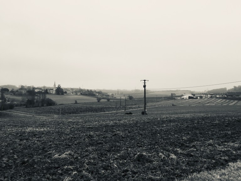 A black and white photo of farm fields with a village church in the distance