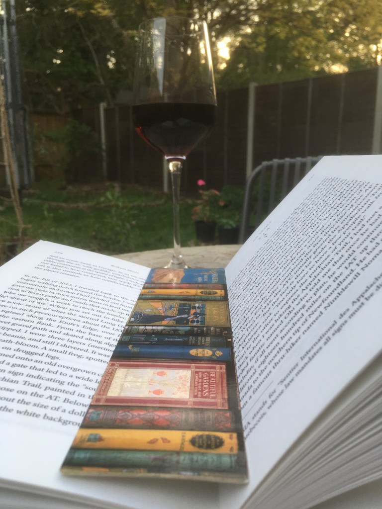 A photo of an open book and a glass of red wine on a garden table